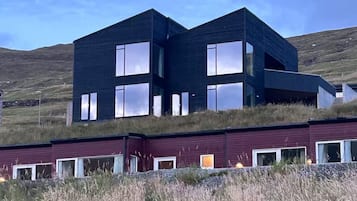Un edificio moderno de dos plantas con grandes ventanales y techo plano, ubicado en un campo cubierto de hierba bajo un cielo despejado.