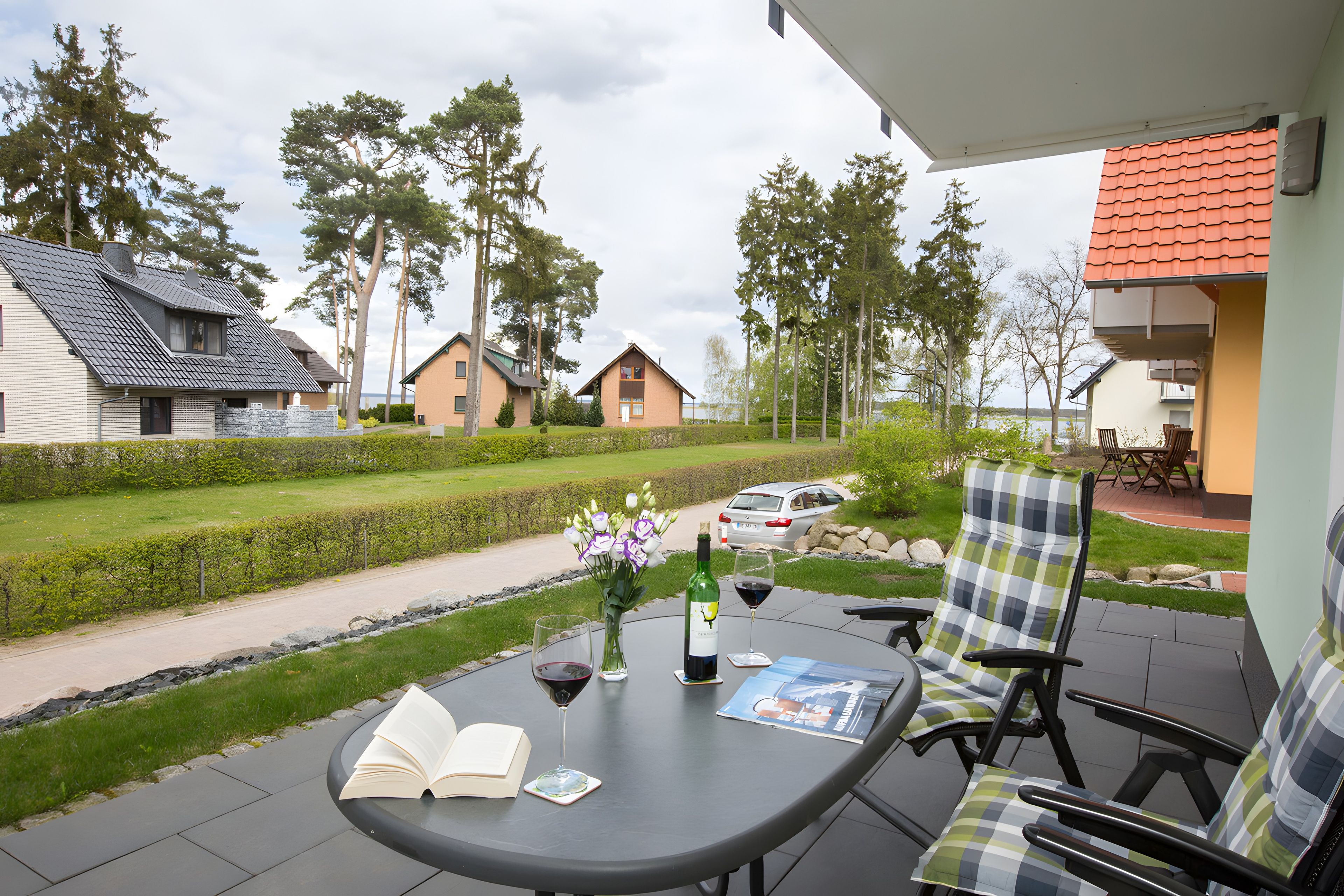 A patio with a table, chairs, a bottle of wine, and an open book.