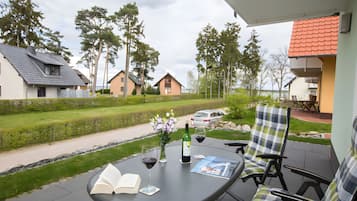 A patio with a table, chairs, a bottle of wine, and an open book.