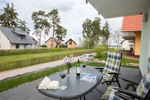 En uteplats med ett bord, stolar, en flaska vin och en öppen bok.