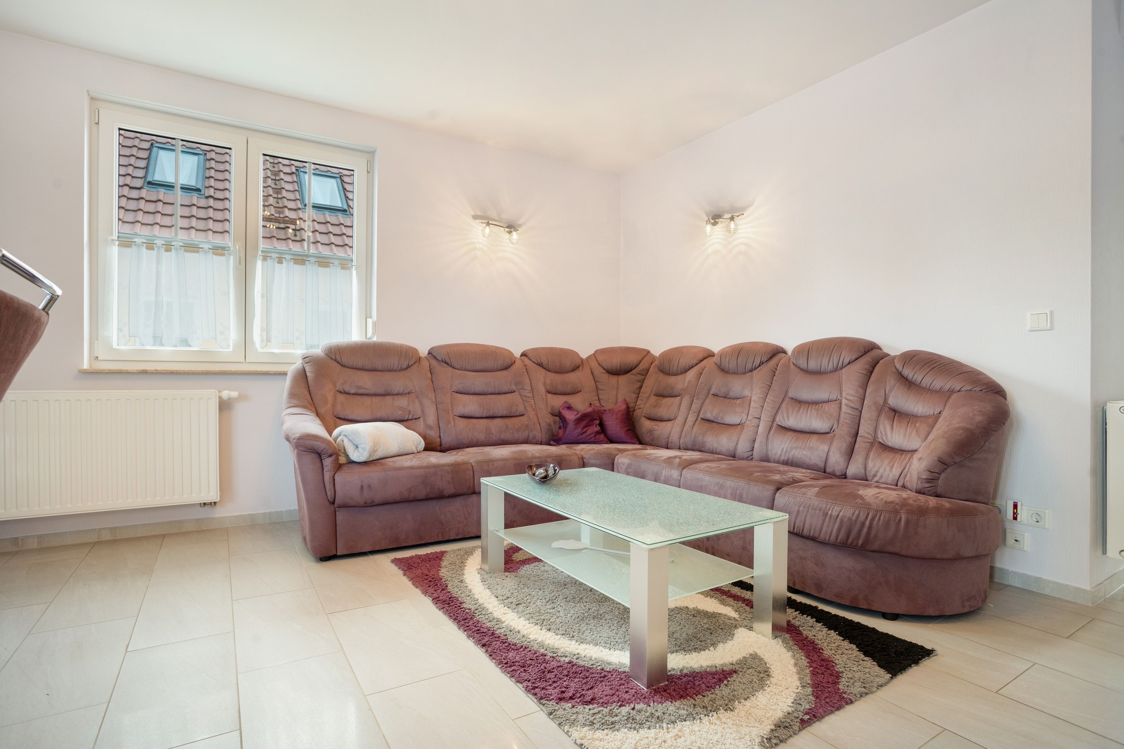 Een moderne woonkamer met een modulaire bank, een glazen salontafel en een kamerkleed met patroon.