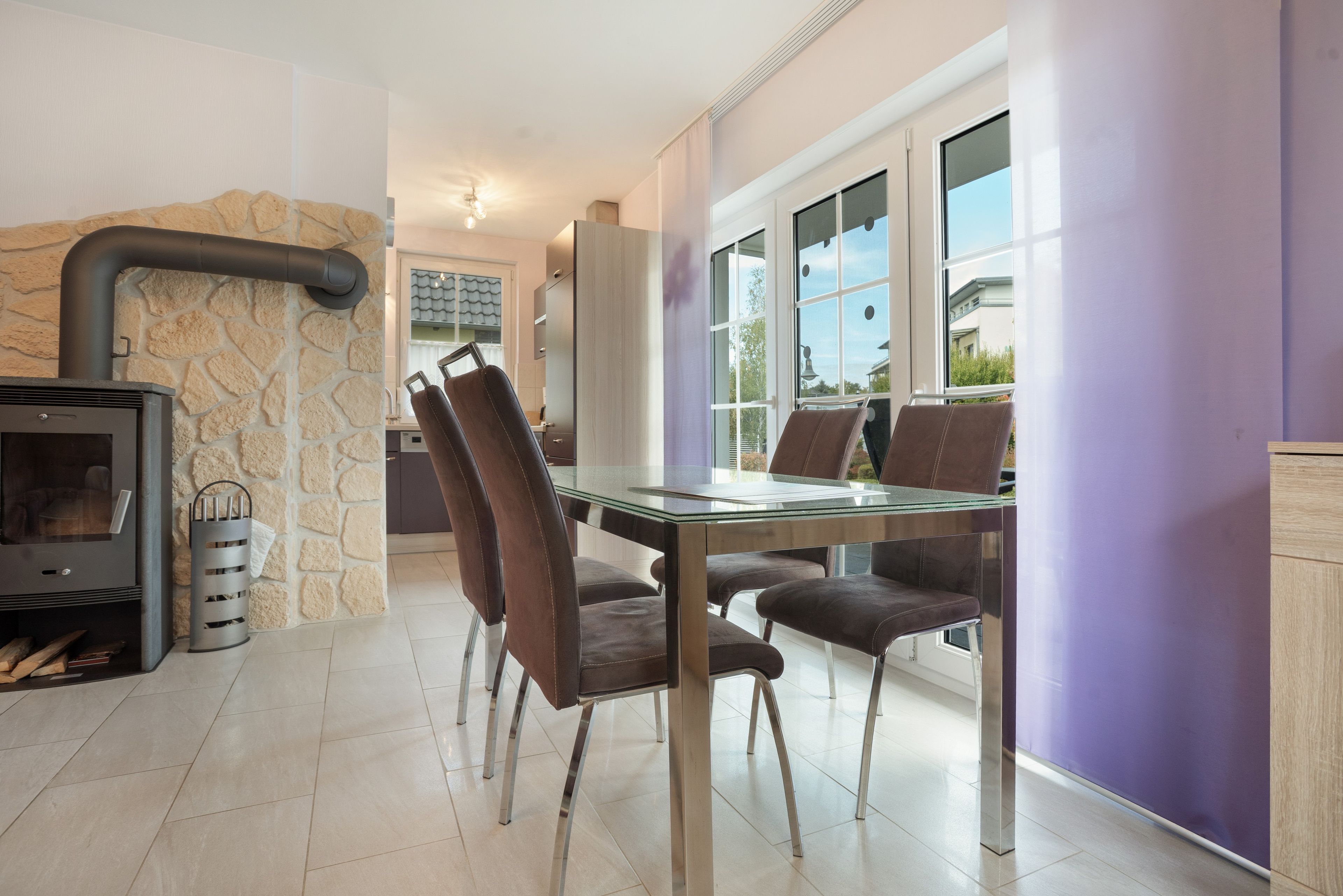 Een moderne keuken met een stenen muur, een inbouwfornuis en een eethoek met een glazen tafel en lederen stoelen.