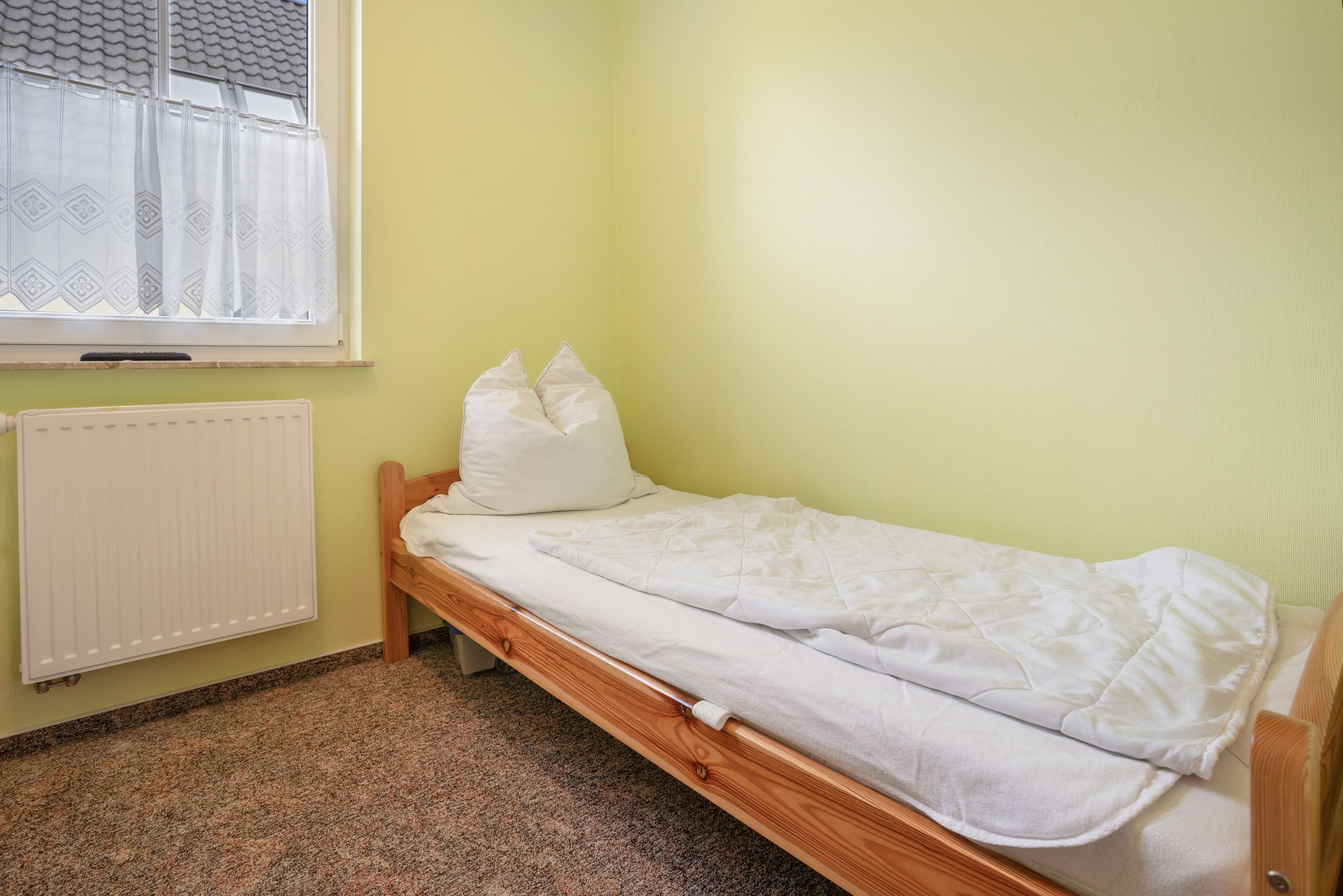 Een eenpersoonsbed met houten frame in een kamer met een radiator en een raam met gordijnen met een patroon.