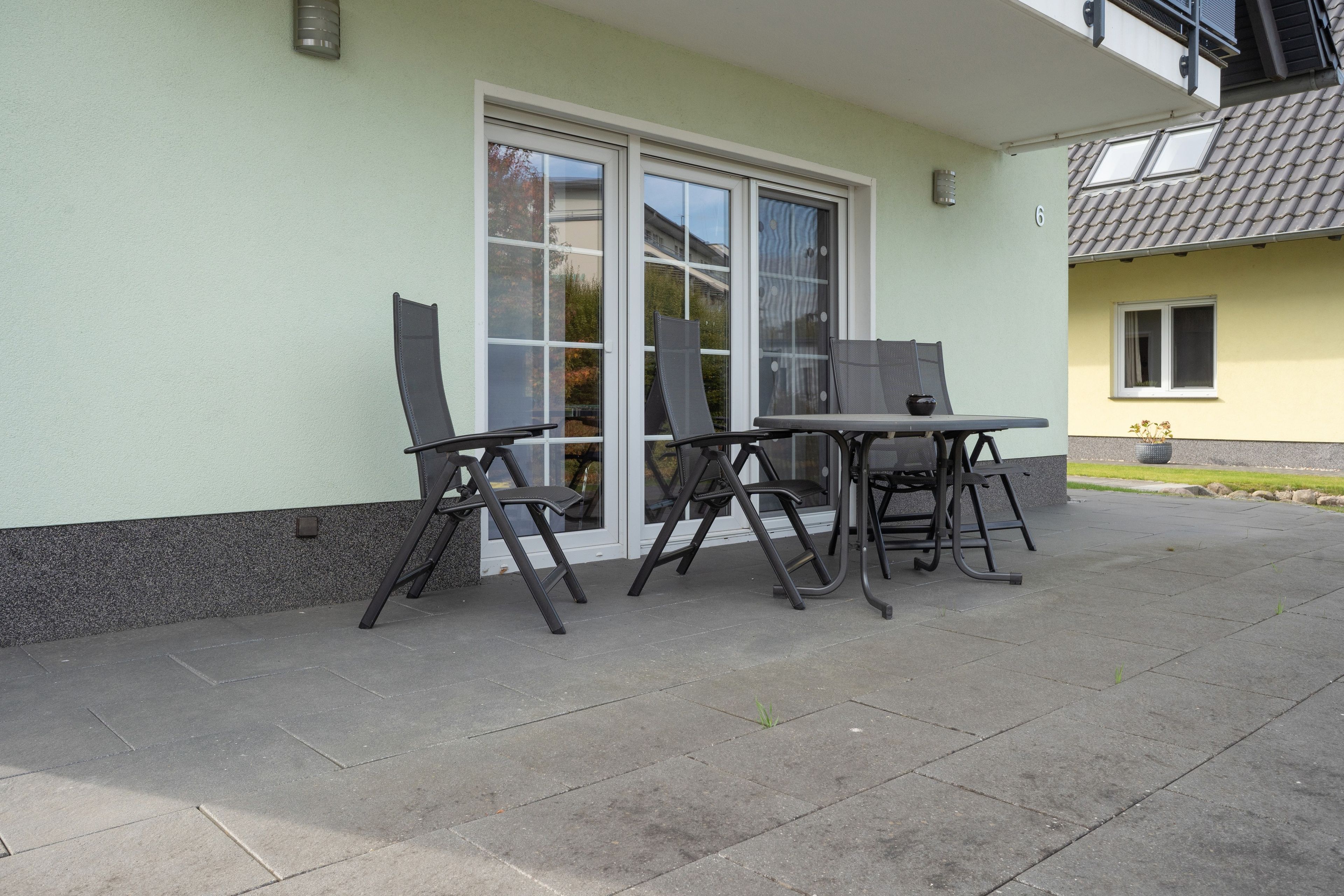 Een terras met een tafel en stoelen, een schuifpui en een kleine tuin.