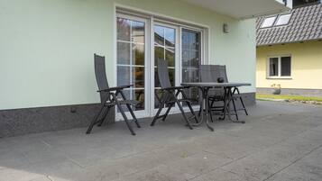 Een terras met een tafel en stoelen, een schuifpui en een kleine tuin.