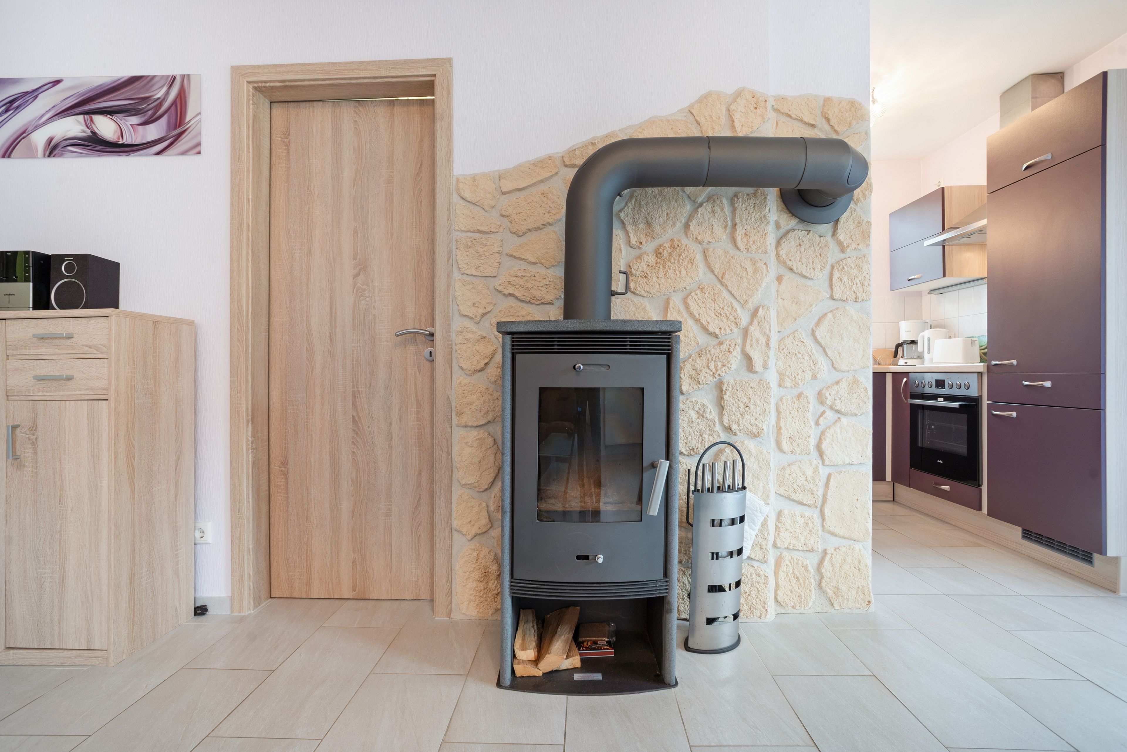 A modern kitchen with a wood-burning stove, stone wall, and wooden cabinets.