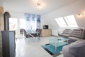 A modern living room with a glass dining table, comfortable seating, a fireplace, and a view of the outdoors. - Apartment 'U 6 OG Biber' with Sea View, Shared Garden and Wi-Fi (Röbel/Müritz)
