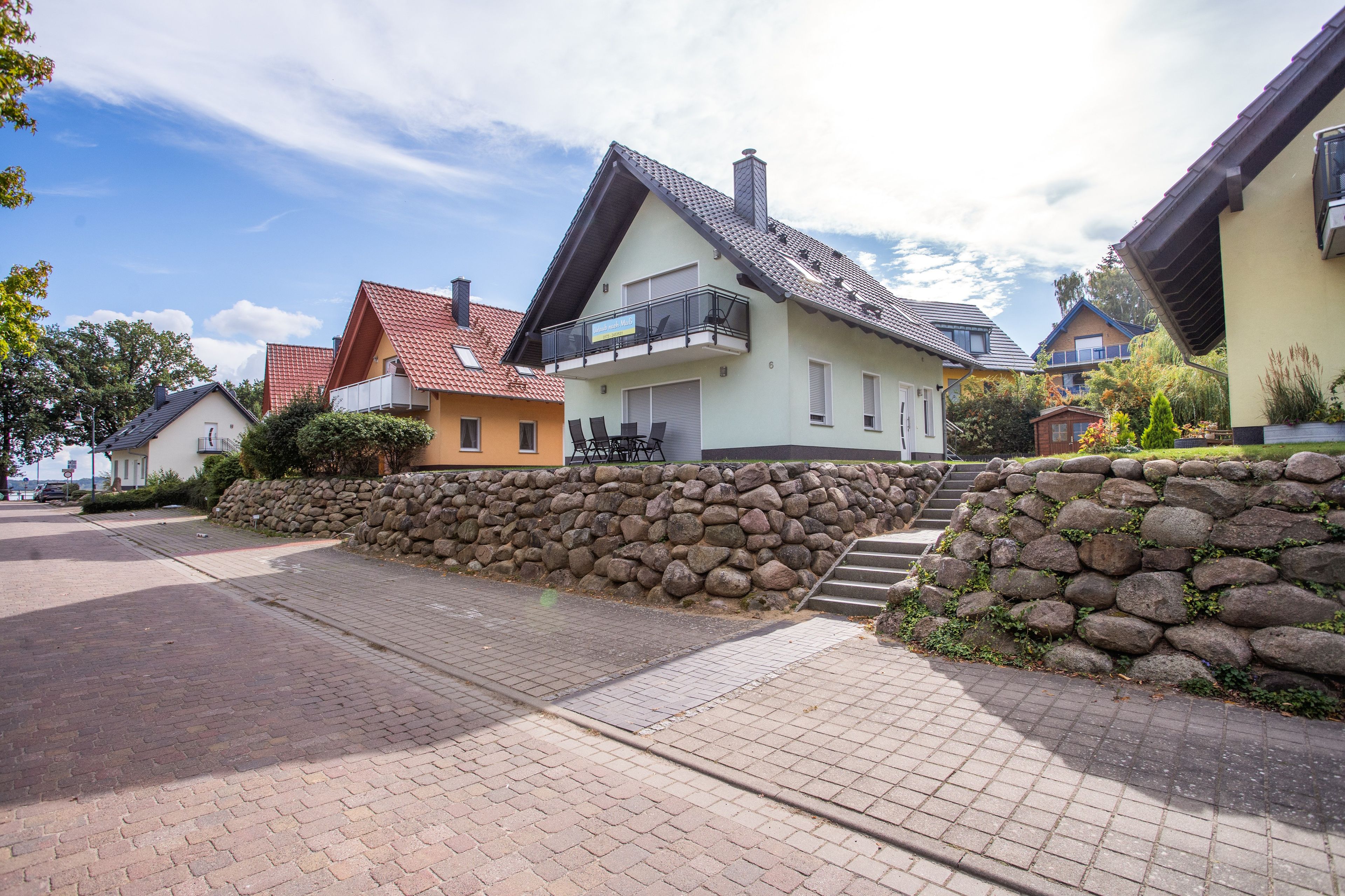 Eine Wohnstraße mit Häusern, einer Steinmauer und einem gepflasterten Bürgersteig.