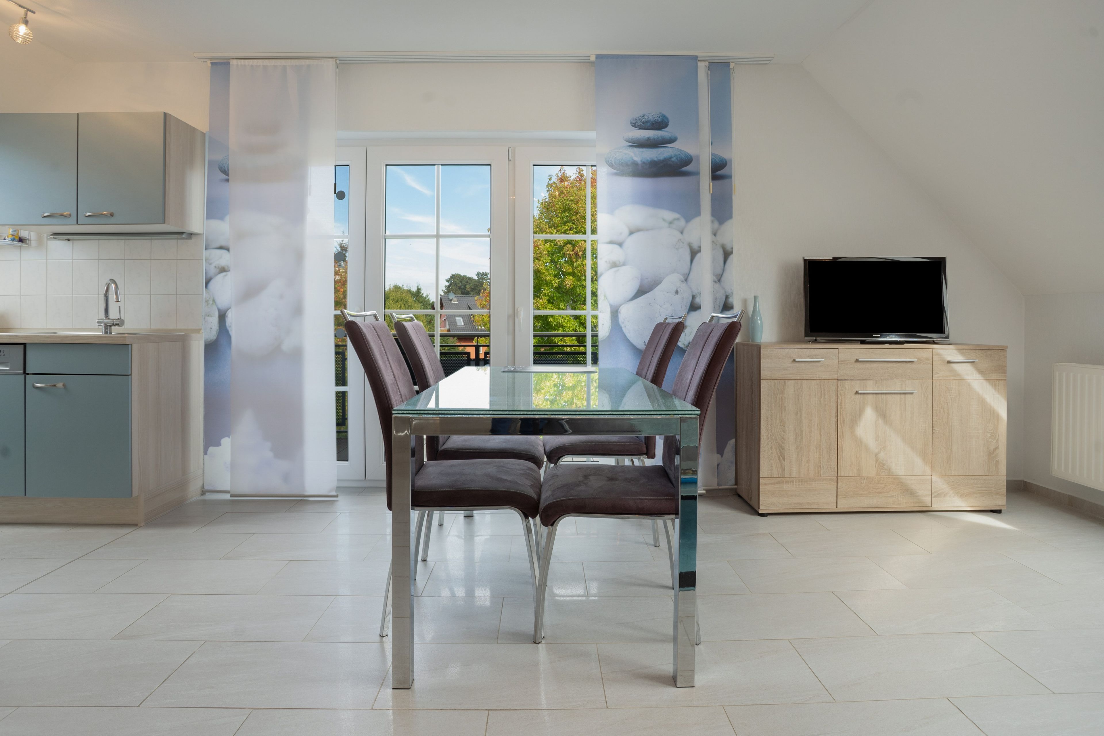 A modern kitchen with a dining area, a TV, and a view through the glass doors.