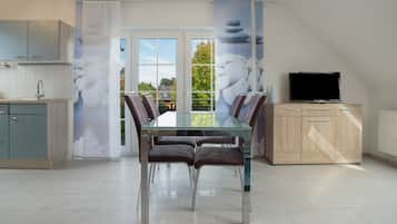 A modern kitchen with a dining area, a TV, and a view through the glass doors.