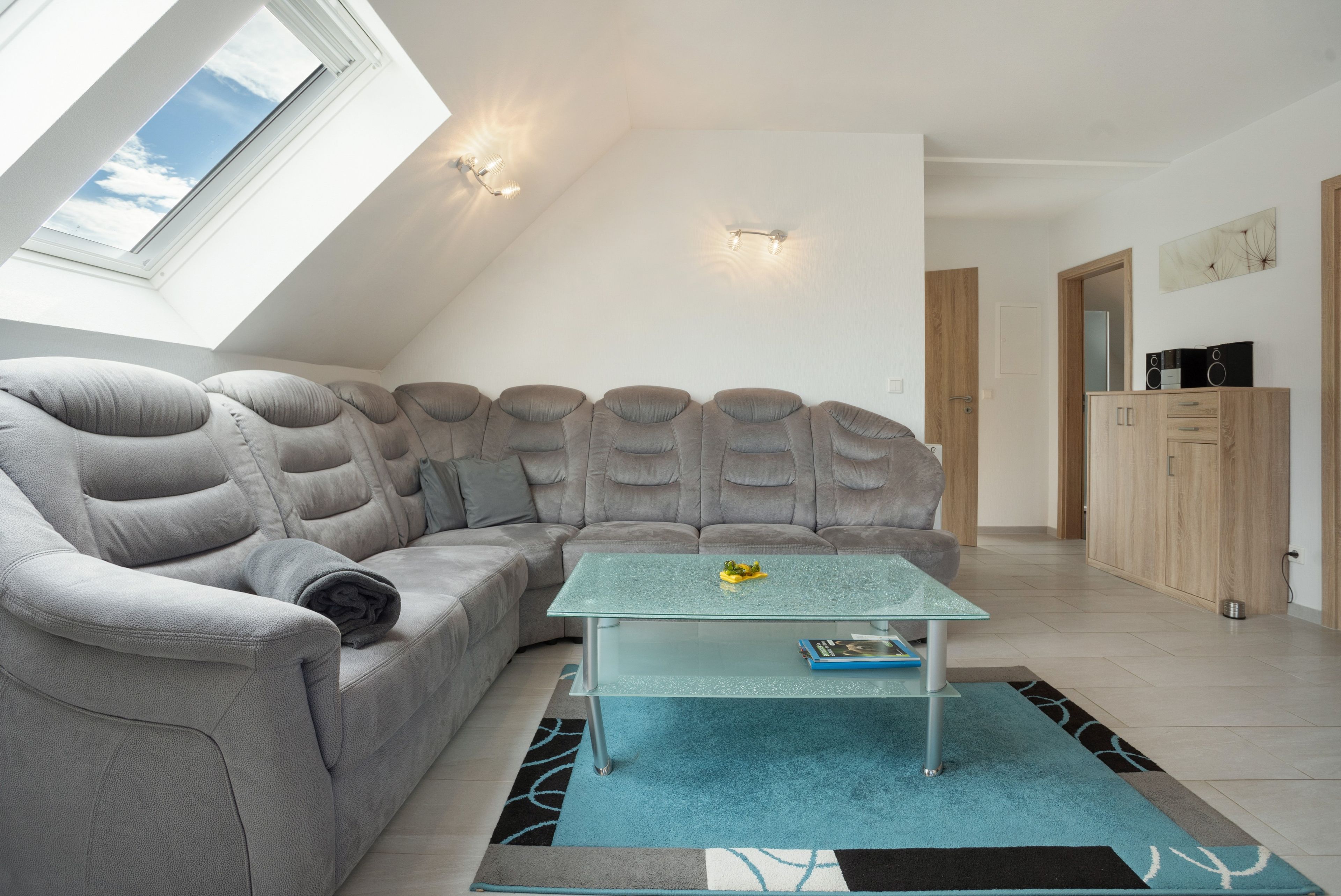 Una sala moderna con un sofá modular, una mesa de centro de vidrio y un tragaluz.