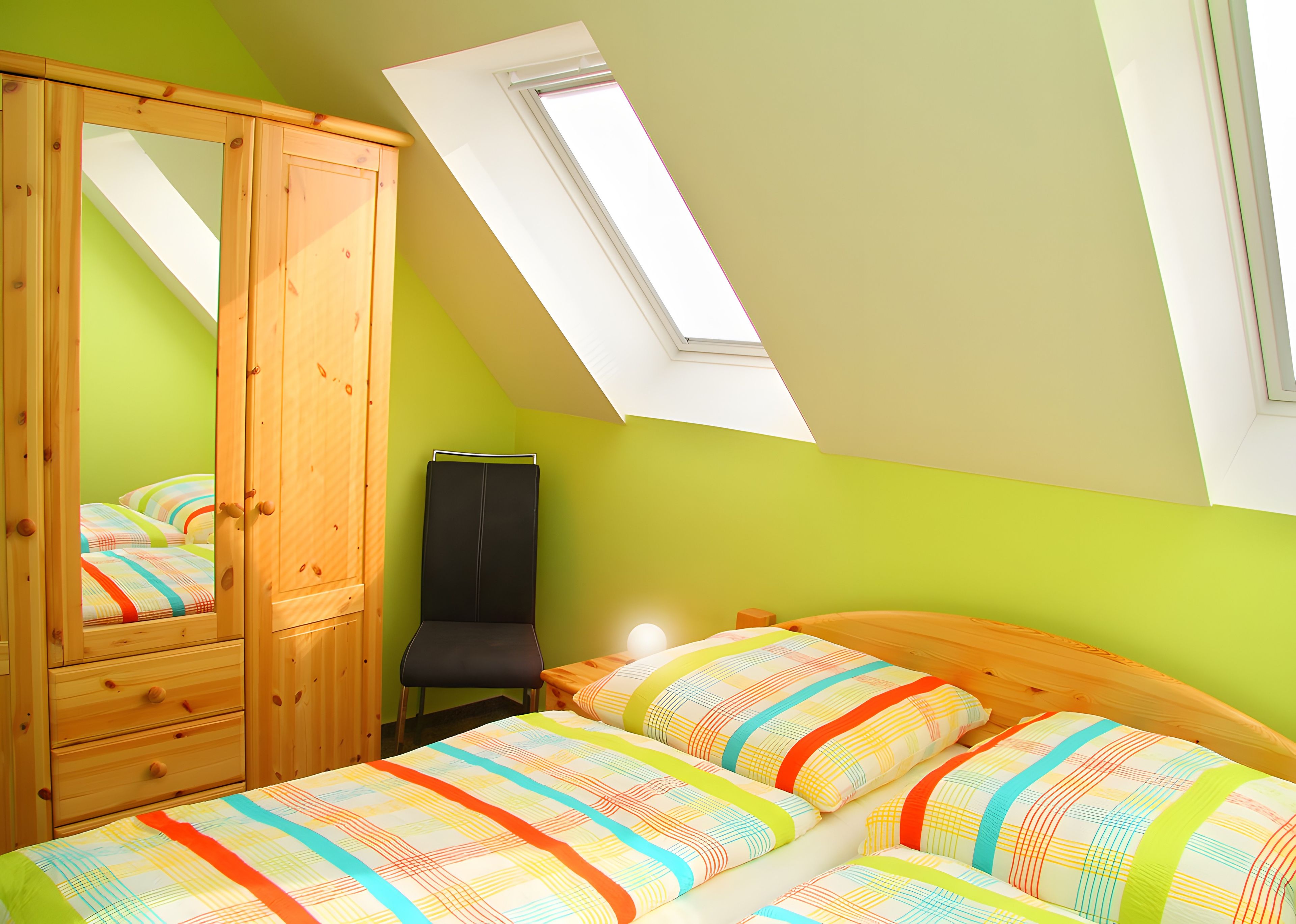 Une chambre avec un plafond en pente, une armoire en bois, un lit avec une literie à rayures et un puits de lumière.