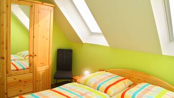 Une chambre avec un plafond en pente, une armoire en bois, un lit avec une literie à rayures et un puits de lumière.