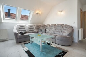 A modern living room with a sectional sofa, a glass coffee table, and a view of the sky through a skylight. - Apartment 'U 6 OG Biber' with Sea View, Shared Garden and Wi-Fi (Röbel/Müritz)