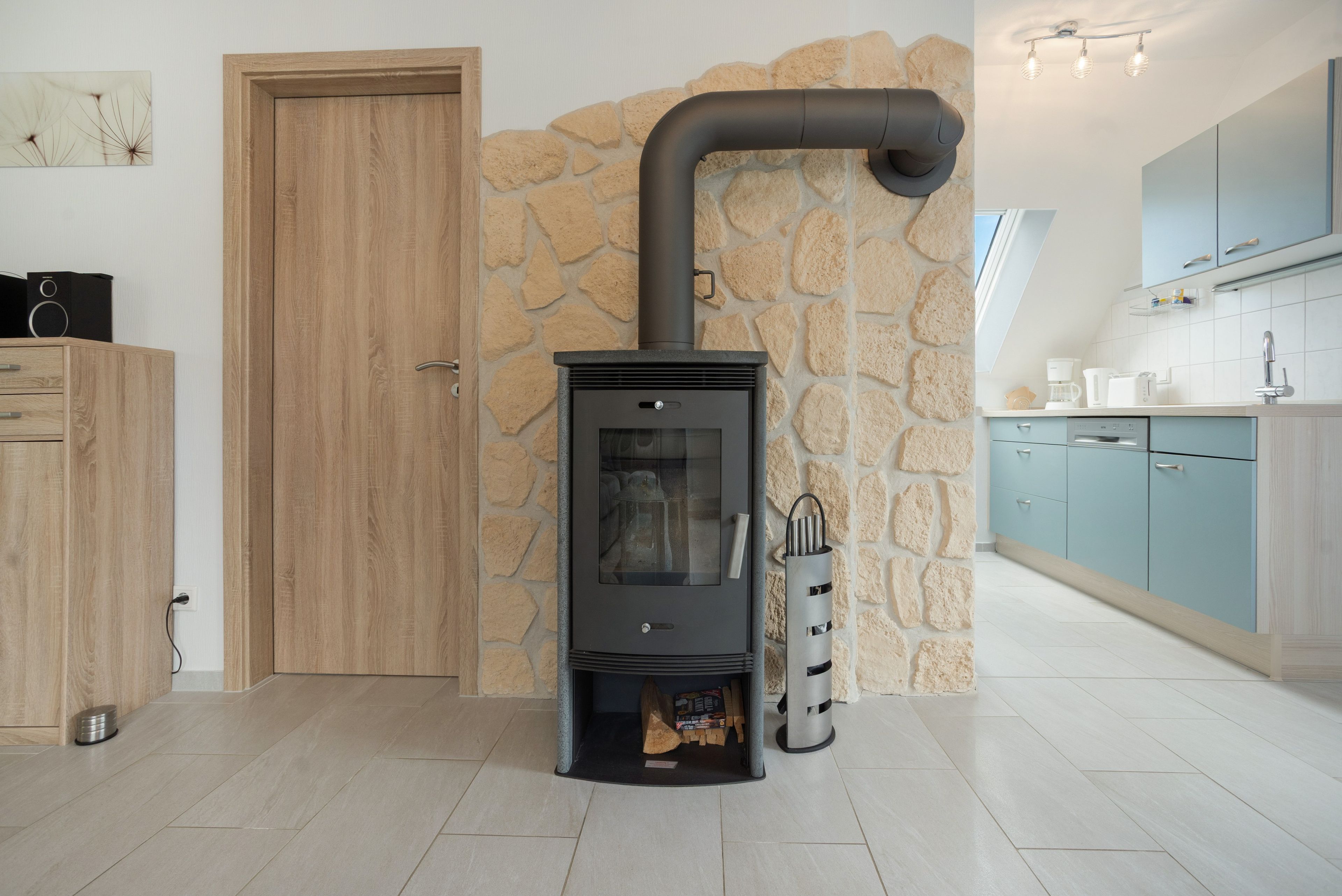 A modern kitchen with a built-in wood stove, stone wall, and light blue cabinets.