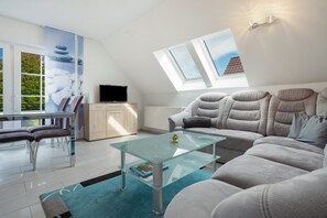 A modern living room with a glass coffee table, grey sofa, and a TV on a wooden cabinet. - Apartment 'U 6 OG Biber' with Sea View, Shared Garden and Wi-Fi (Röbel/Müritz)