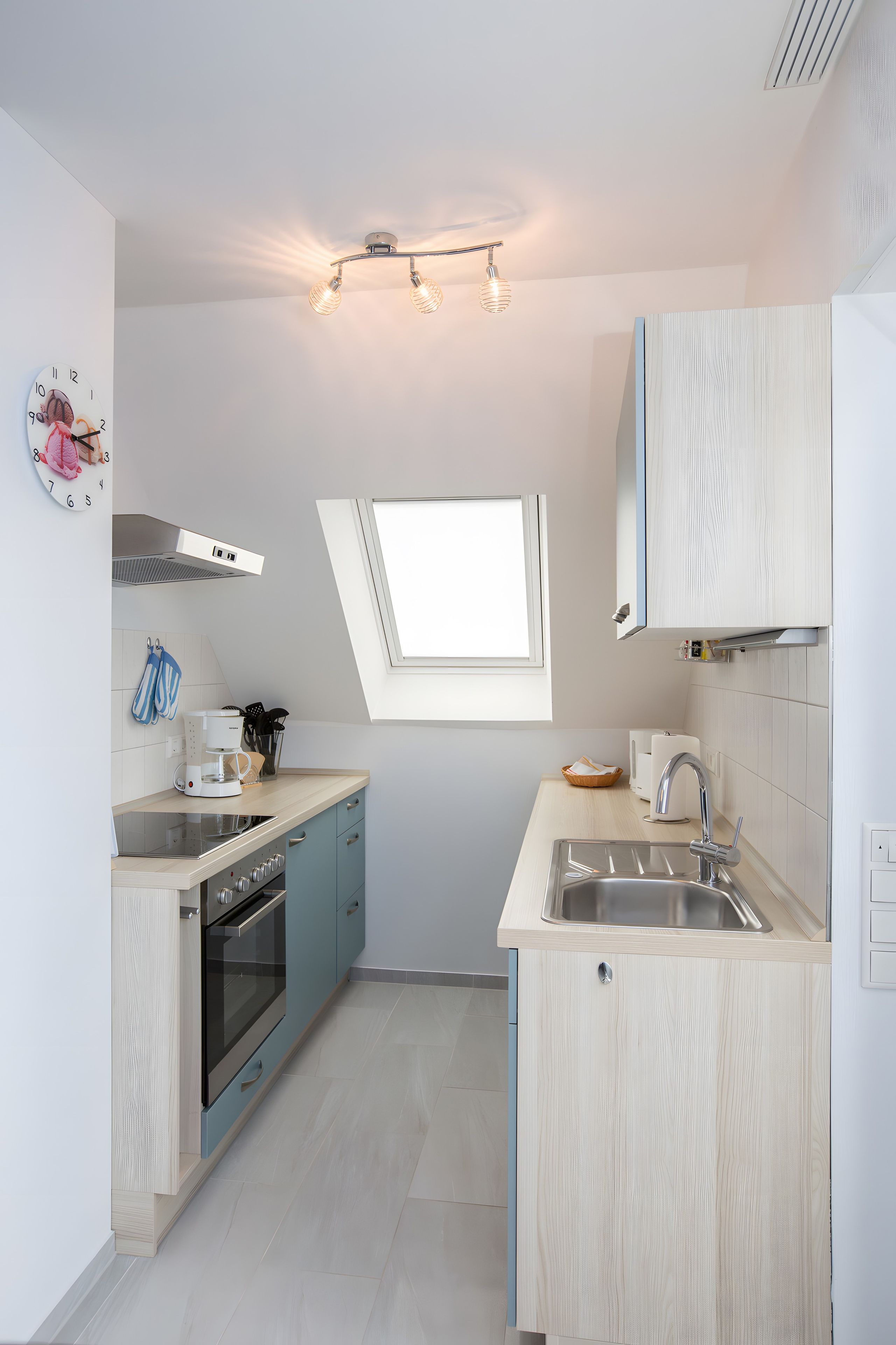 A compact kitchen with a built-in oven, a coffee machine, and a window above the sink.
