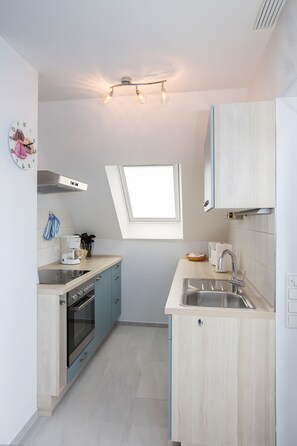 A compact kitchen with a built-in oven, a coffee machine, and a window above the sink. - Apartment 'U 6 OG Biber' with Sea View, Shared Garden and Wi-Fi (Röbel/Müritz)