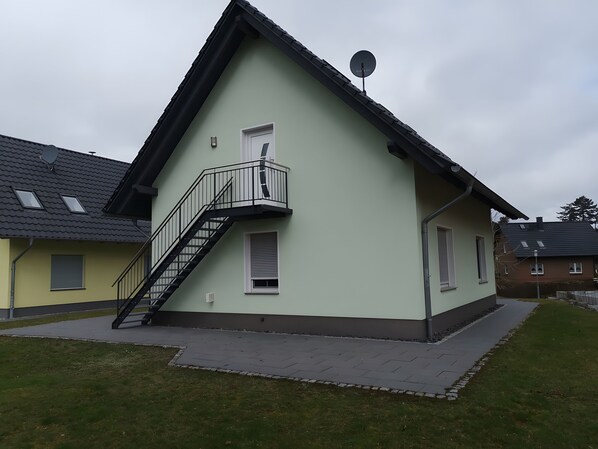 Ein zweistöckiges Haus mit einem Balkon, einer Satellitenschüssel und einer sichtbaren Treppe.