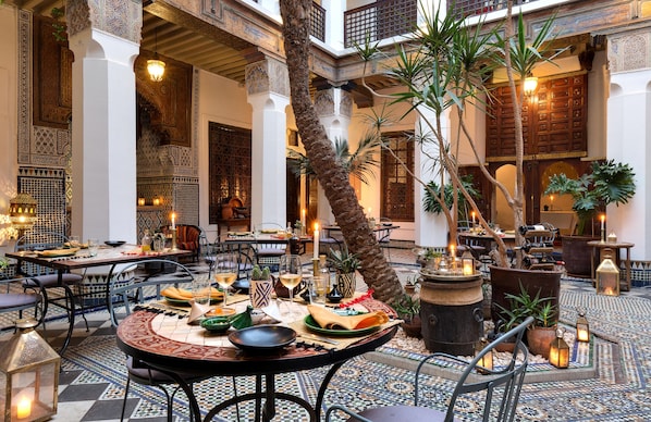 Un comedor interior con mesas dispuestas para comidas, rodeado de muros y columnas ornamentales.