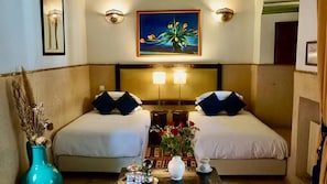 Habitación de hotel con dos camas, una mesita de noche, un florero con flores y un cuadro en la pared.