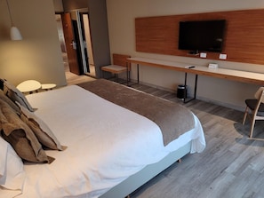 A hotel room with a large bed, a desk with a flat-screen TV, and a chair.
