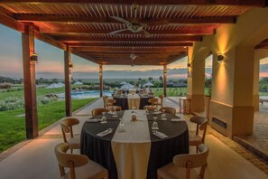 An outdoor dining area with tables set for a meal, surrounded by chairs, with a view of a pool and landscape. - Hotel Termas Victoria (Victoria)