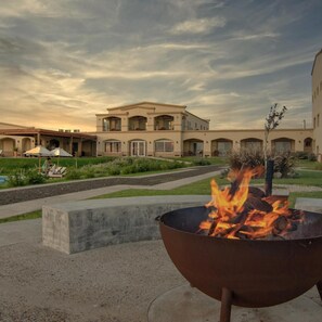 A building with a fire pit in the foreground, a pool, and a covered patio area. - Hotel Termas Victoria (Victoria)