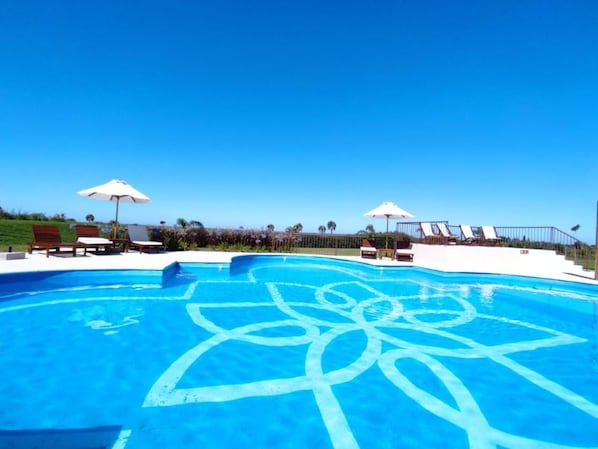 A clear blue swimming pool with a geometric design, surrounded by lounge chairs and umbrellas.