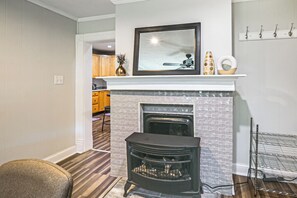 A living room with a fireplace, a dining area in the background, and a hallway leading to another room. - Modern 1BR: Queen Bed, Coffee Bar & Walkin Shower (Parkersburg)