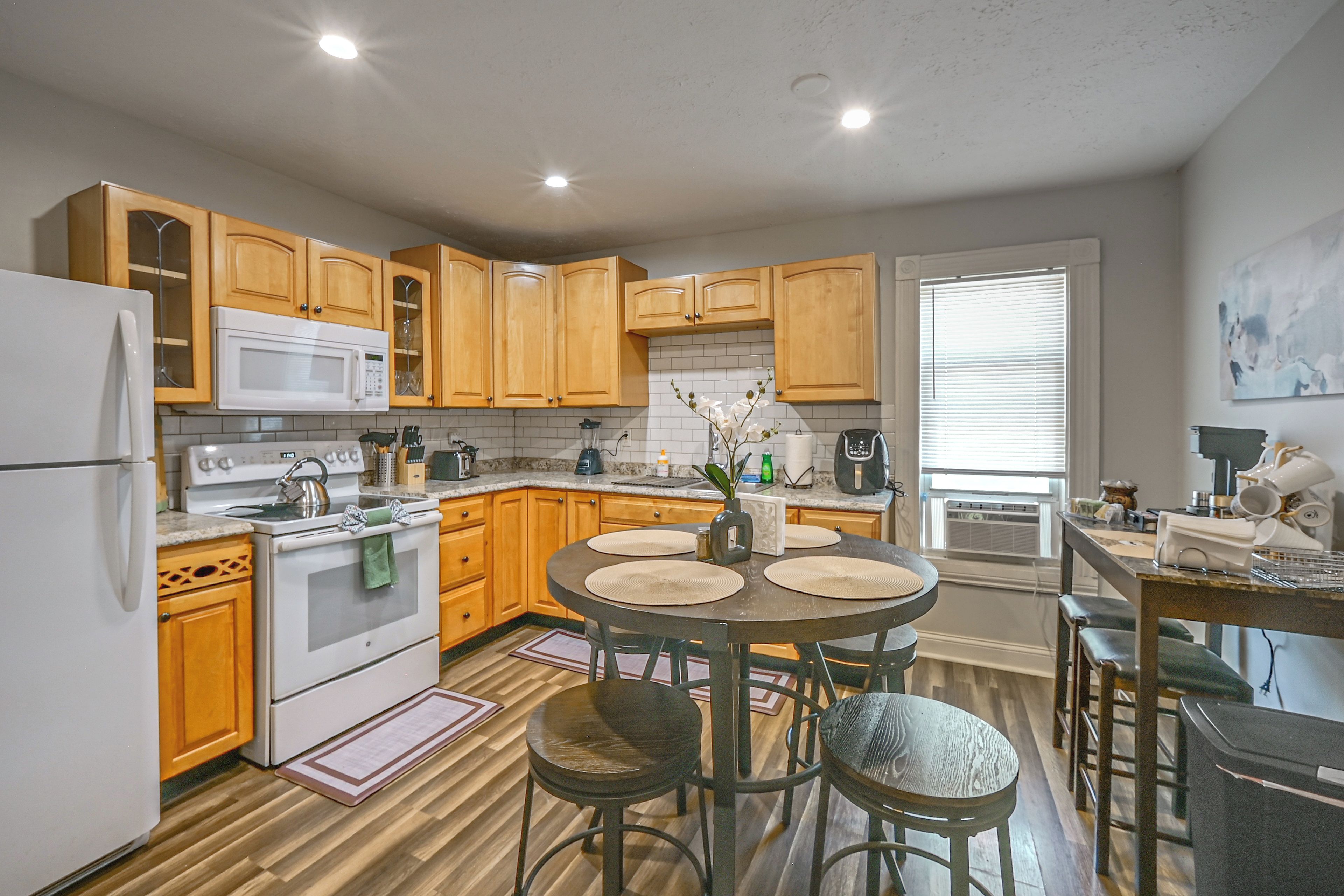 A modern kitchen with wooden cabinets, a white refrigerator, a stove, and a dining area with a table and chairs.