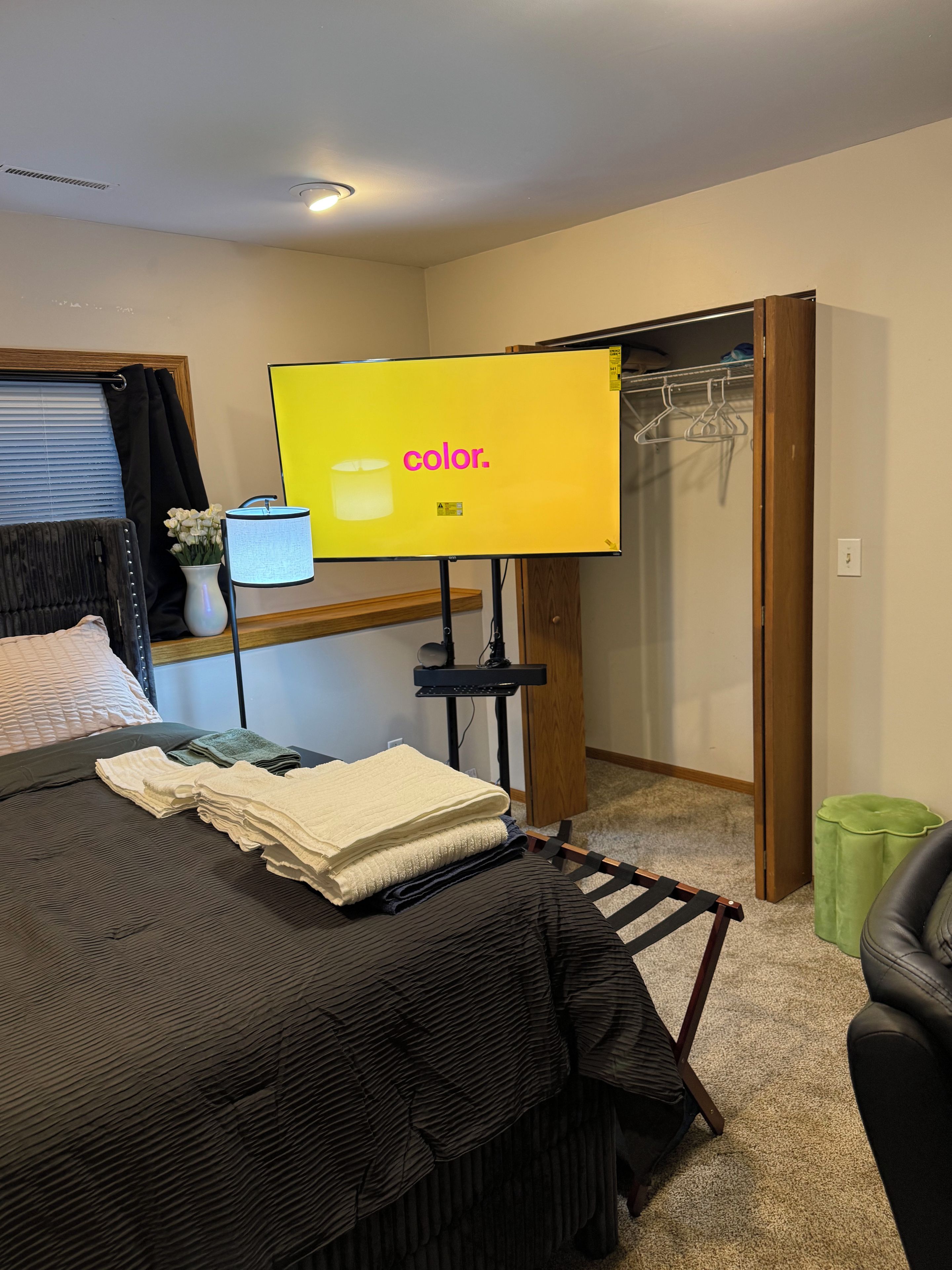 A bedroom with a bed, a TV on a stand, a closet, and a green trash bin.