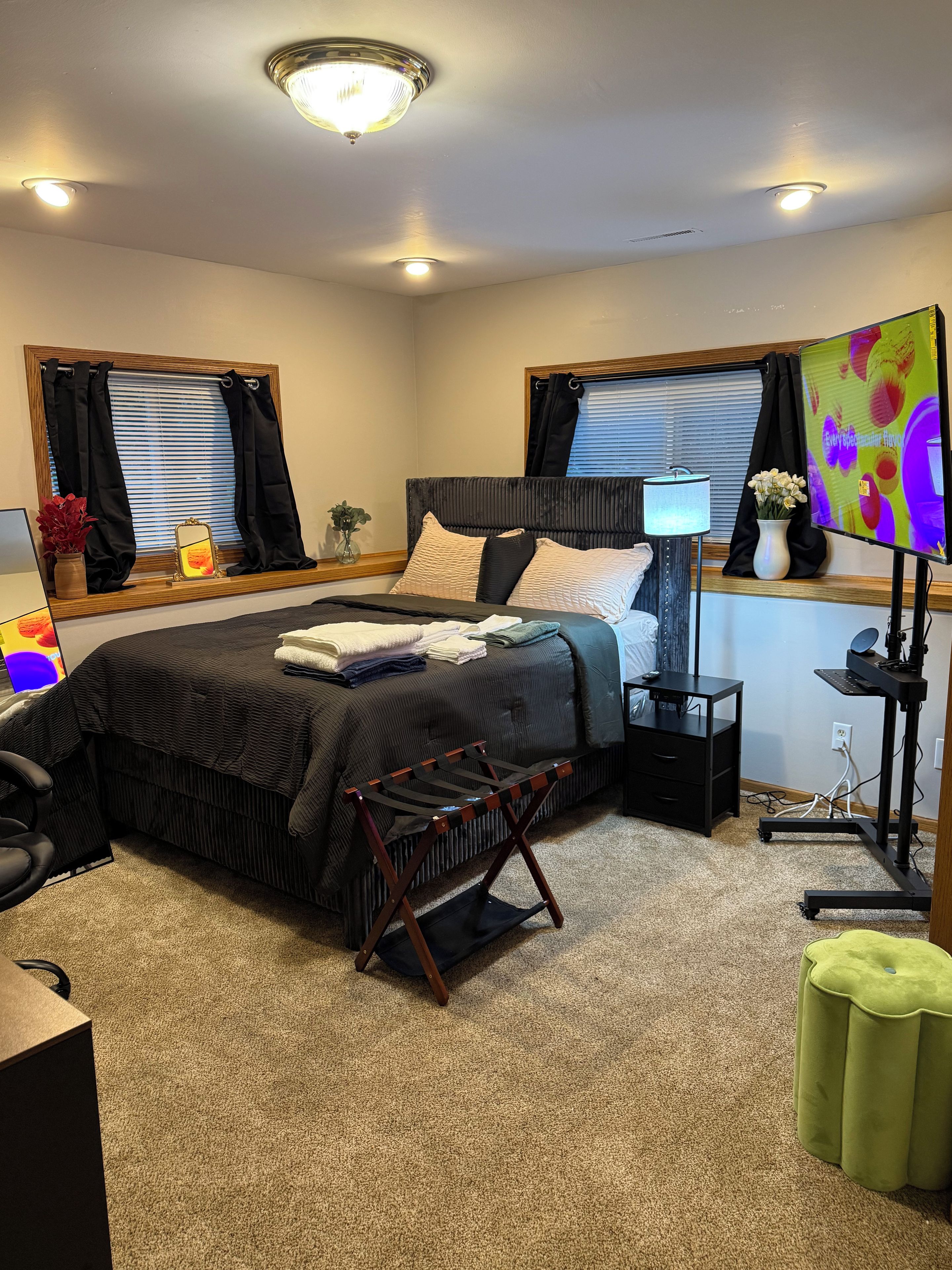 Une chambre à coucher comprenant un lit, un bureau, une chaise, une lampe, un téléviseur et une fenêtre avec des rideaux.