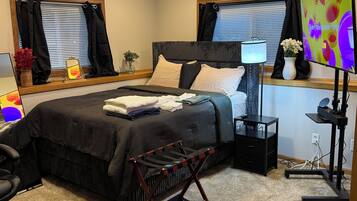 Une chambre à coucher comprenant un lit, un bureau, une chaise, une lampe, un téléviseur et une fenêtre avec des rideaux.