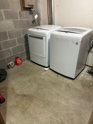 Two white front-loading washing machines in a laundry area with a concrete floor, a brick wall, and a door in the background. - Charming 2-bedroom Downstairs in fantastic Saint Paul with AC (Saint Paul)