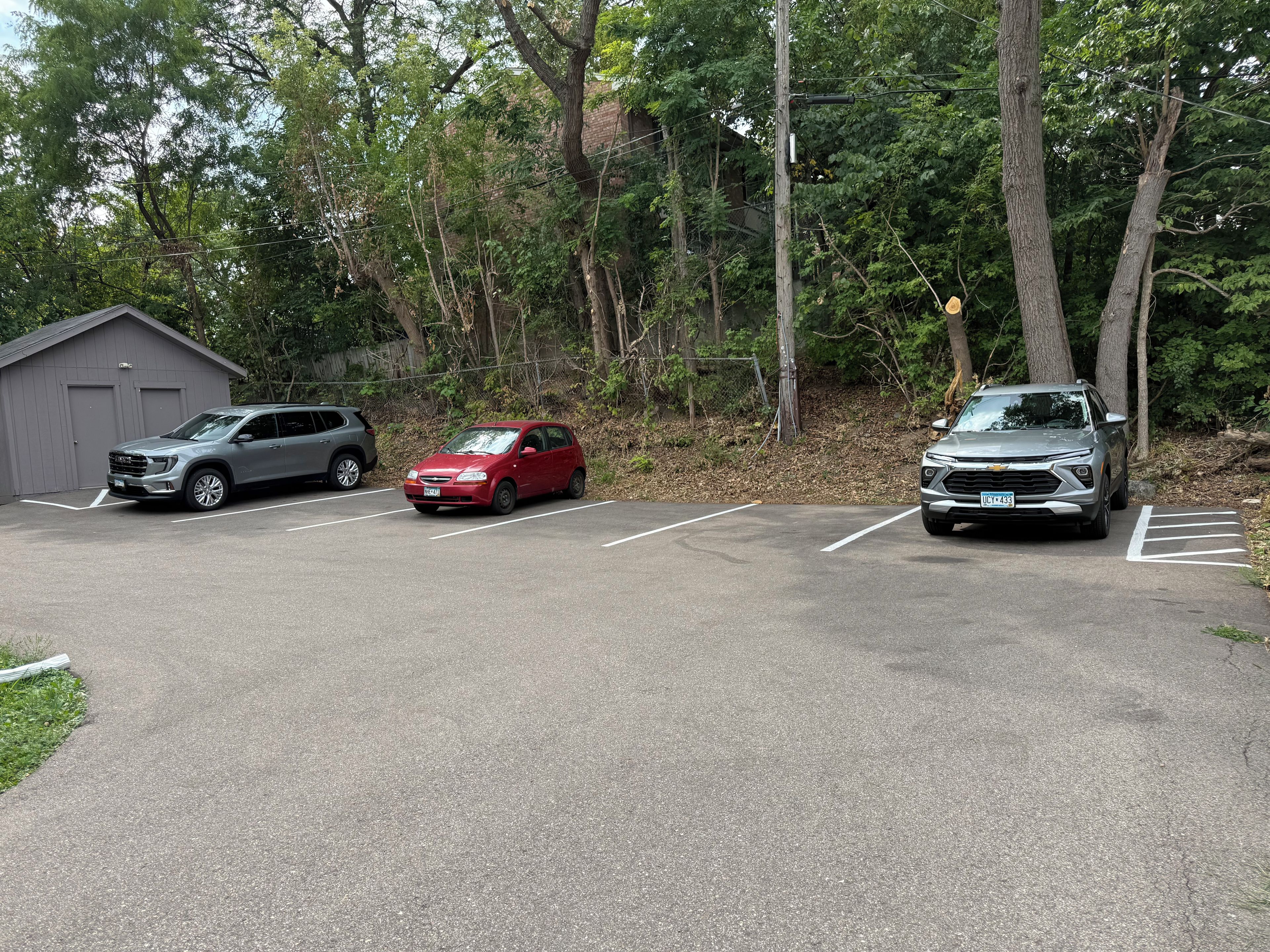 A parking lot with three vehicles, a building, and trees in the background.