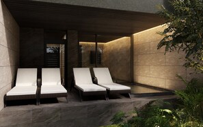 Un área lounge moderna al aire libre con tres sillones y un banco integrado, rodeada de muros de piedra y vegetación.