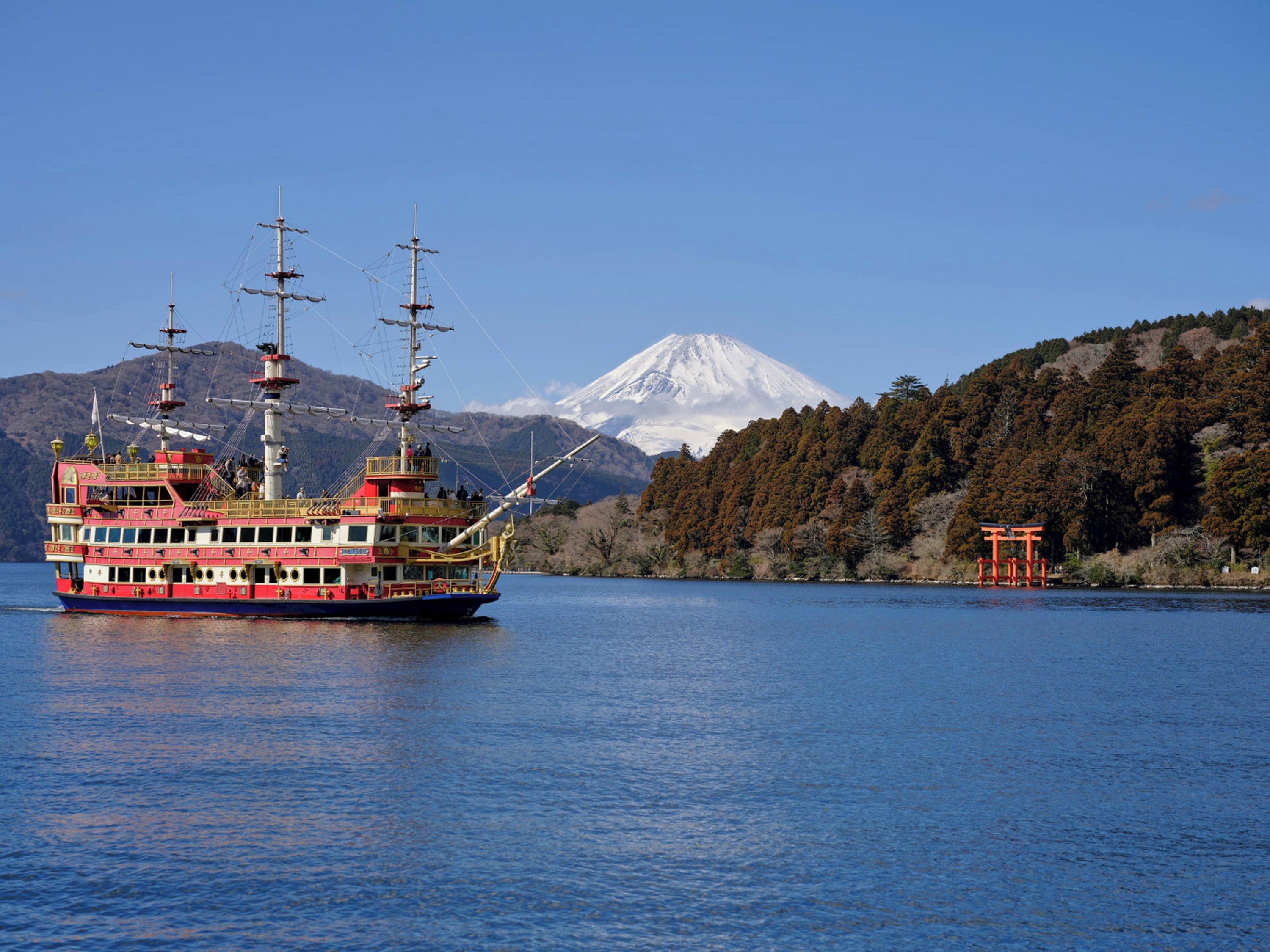 Un gran ferry de varias cubiertas y múltiples mástiles navegando sobre aguas tranquilas, con una montaña nevada al fondo.