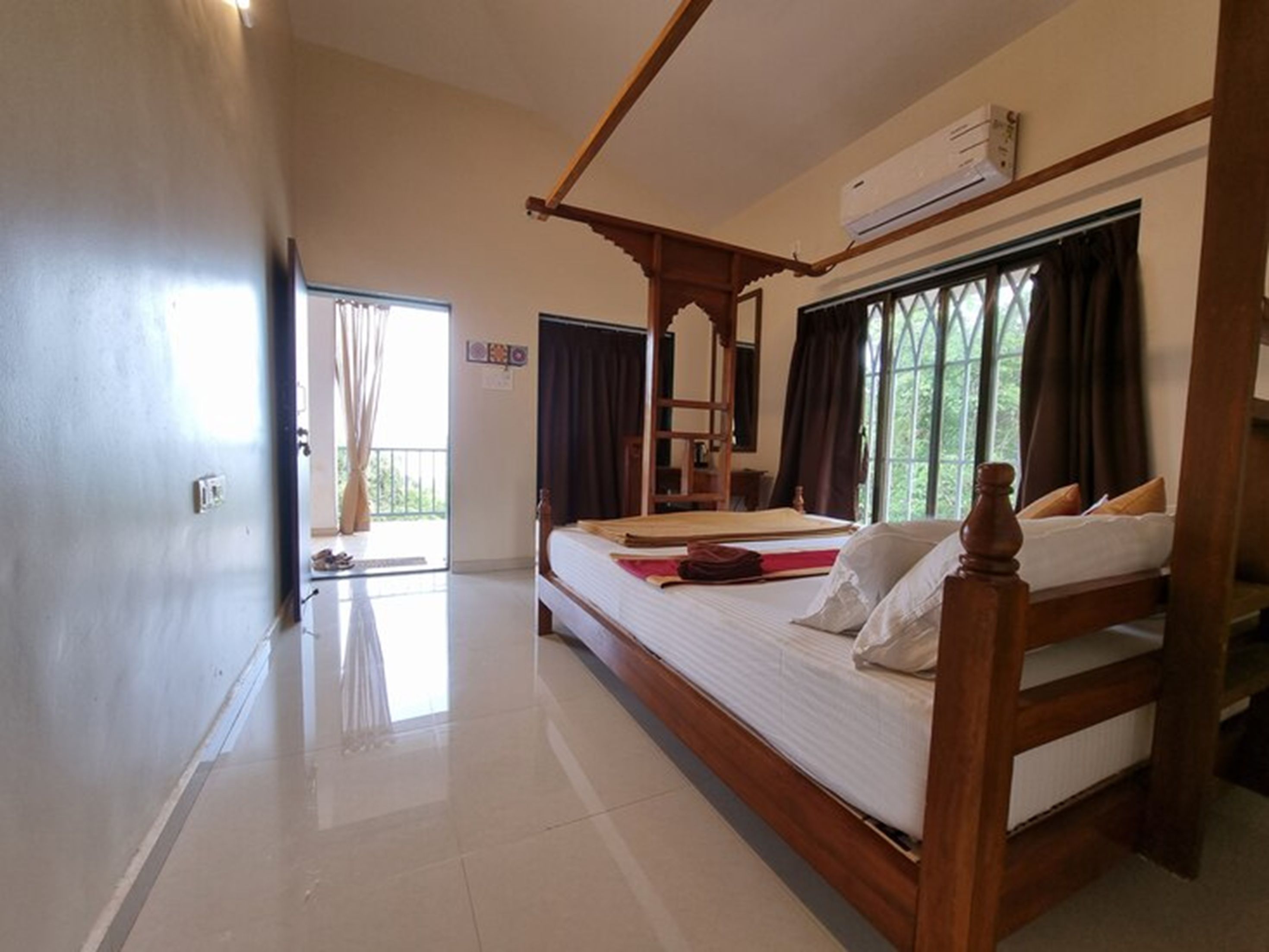 Quarto de hotel com uma cama de madeira com dossel, uma varanda com vista e um ar condicionado na parede.