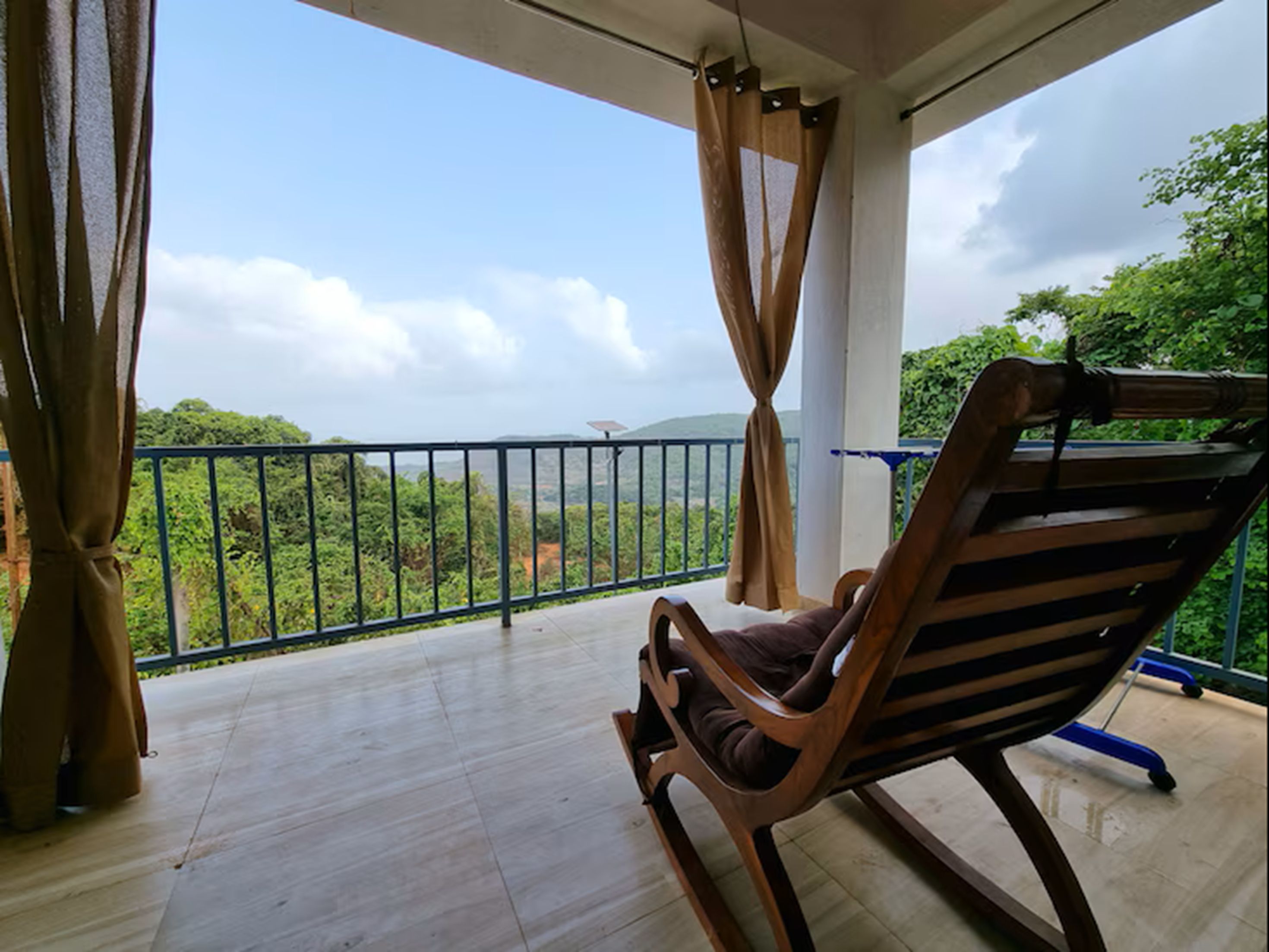 A balcony with a wooden chair, a metal railing, and a view of greenery.
