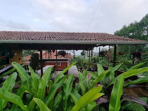 A covered outdoor area with a tiled roof, surrounded by lush green plants. - Thavika Sky County - Dapoli (Dapoli)