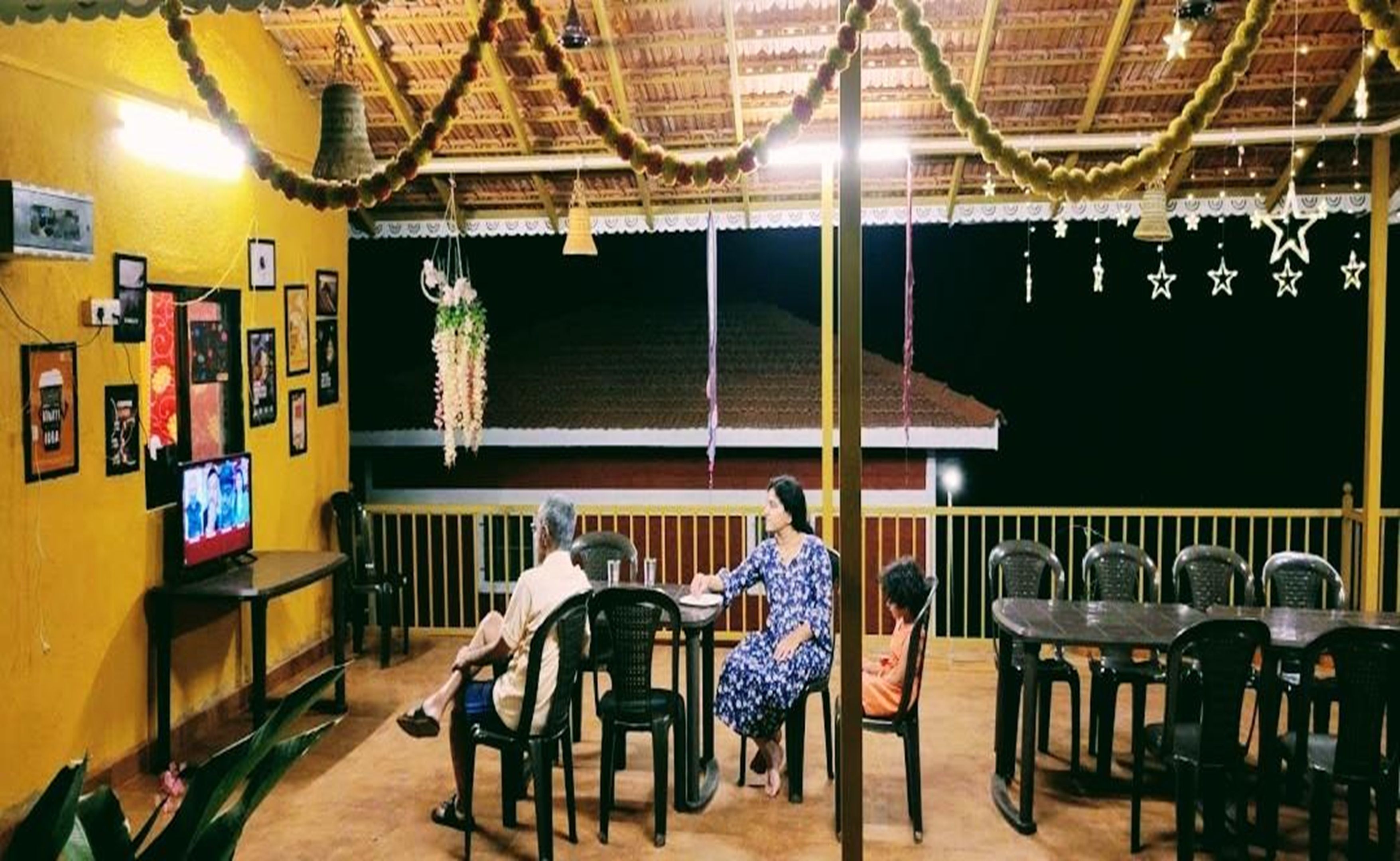 An indoor dining area with a thatched roof, tables, chairs, and a television screen.