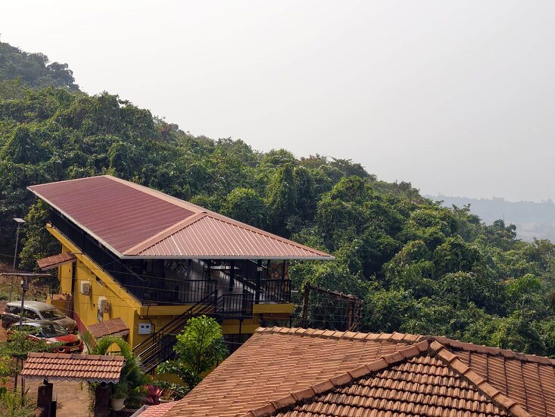 A yellow building with a red roof, surrounded by lush greenery and hills.