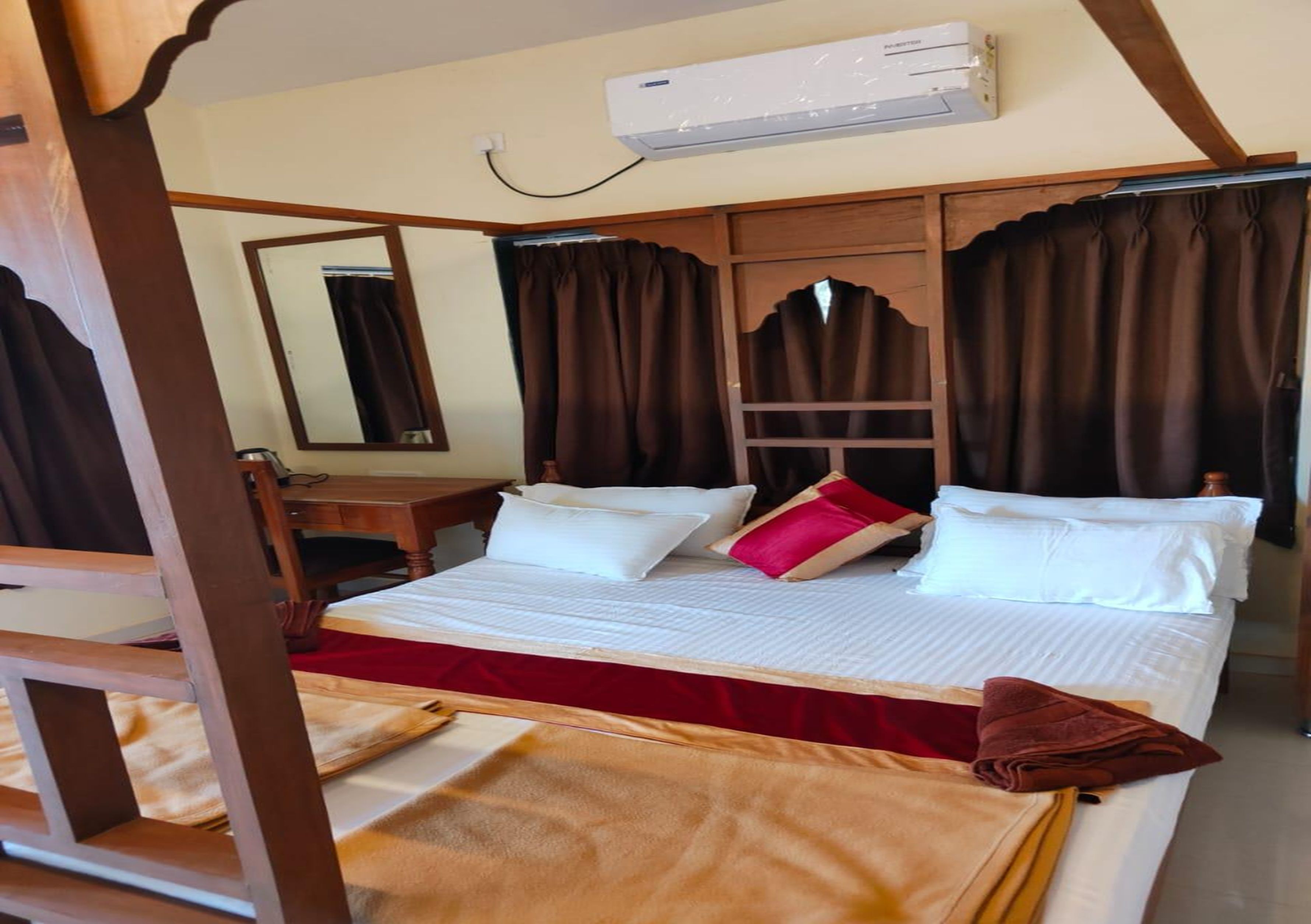 A hotel room with a bed, a desk, a chair, a mirror, and an air conditioning unit.