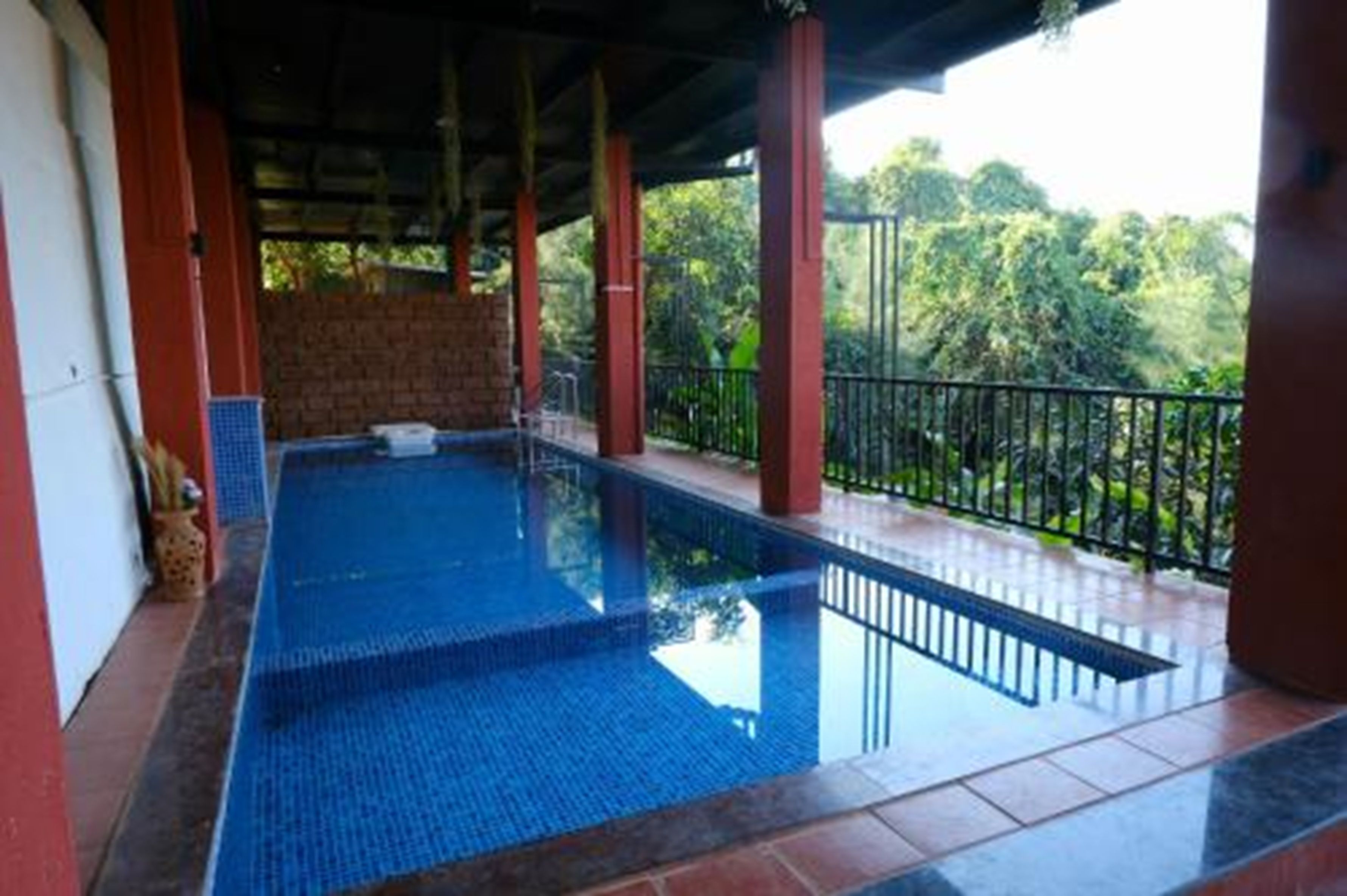 Una piscina con borde de baldosas, rodeada por una barandilla y un área techada con pilares.