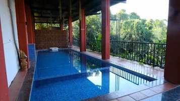 Una piscina con borde de baldosas, rodeada por una barandilla y un área techada con pilares.