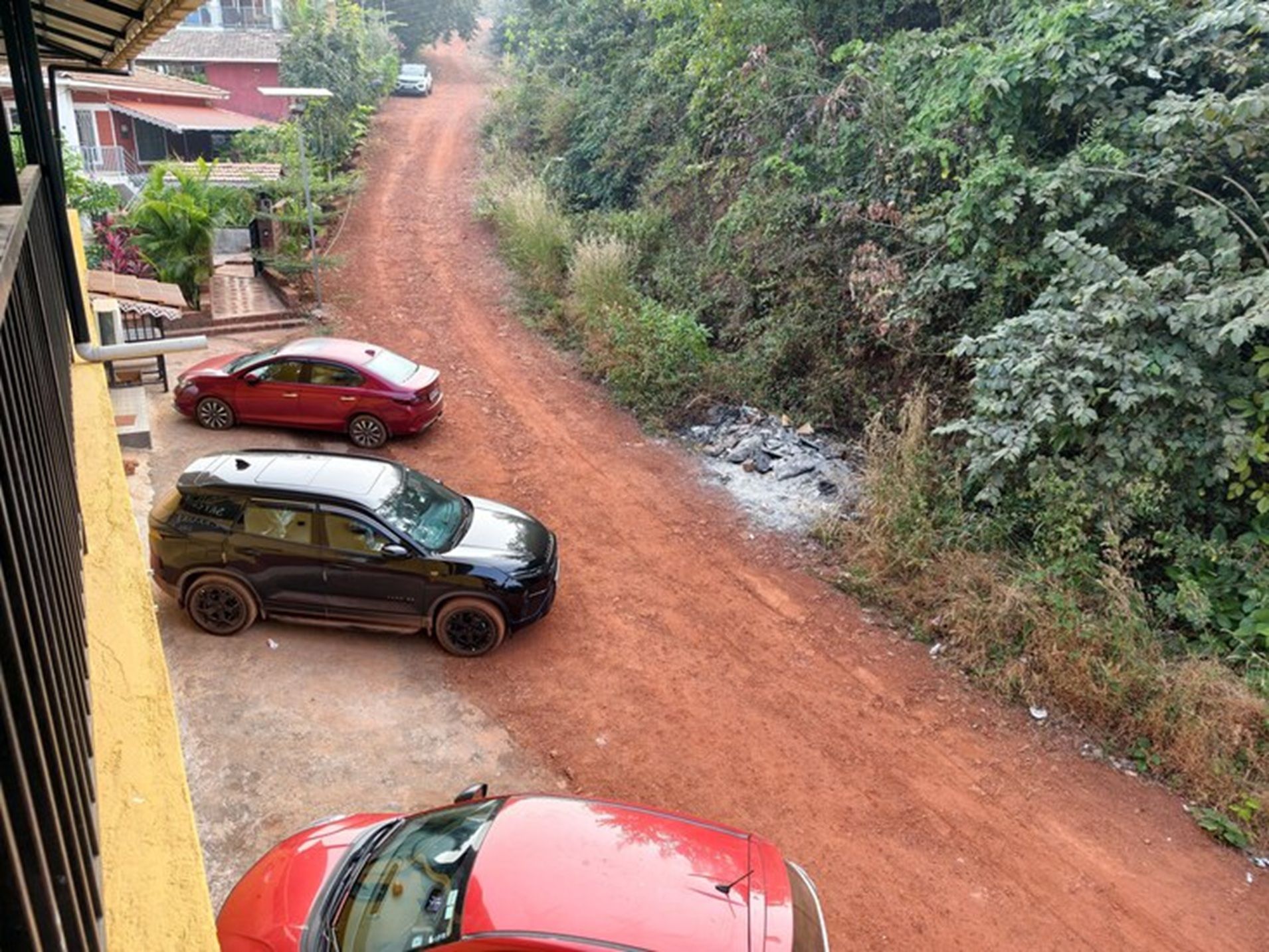 Un camino de tierra con coches aparcados al borde, rodeado de vegetación.