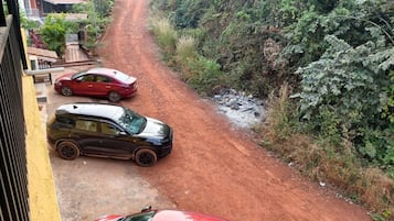 Un camino de tierra con coches aparcados al borde, rodeado de vegetación.