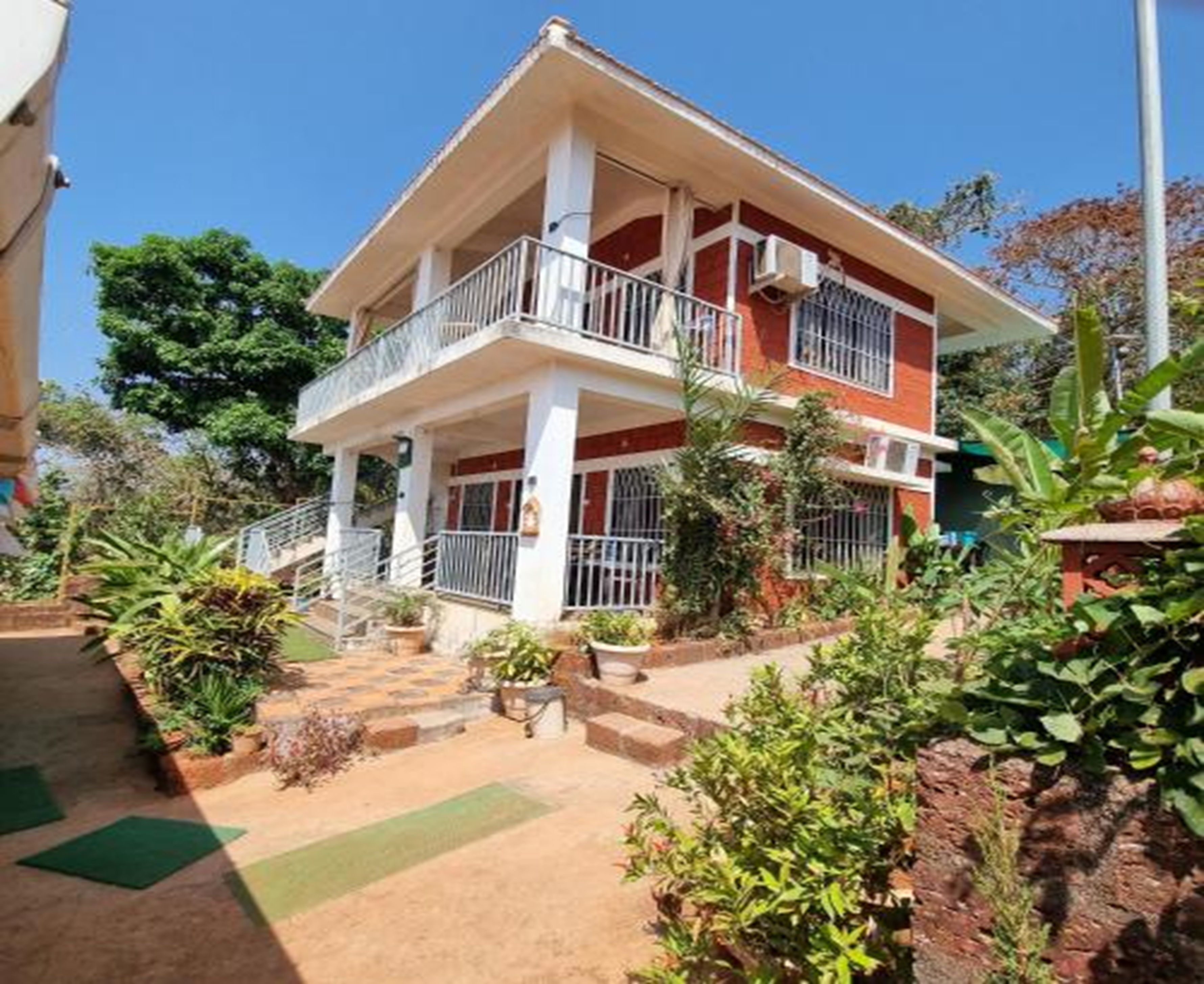 Un immeuble de deux étages doté d’un balcon, entouré de verdure.