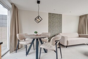A modern living room with a round dining table, four chairs, a sofa, and a pendant light. - Piet Mondriaanpad 3 West Chapel (Westkapelle)